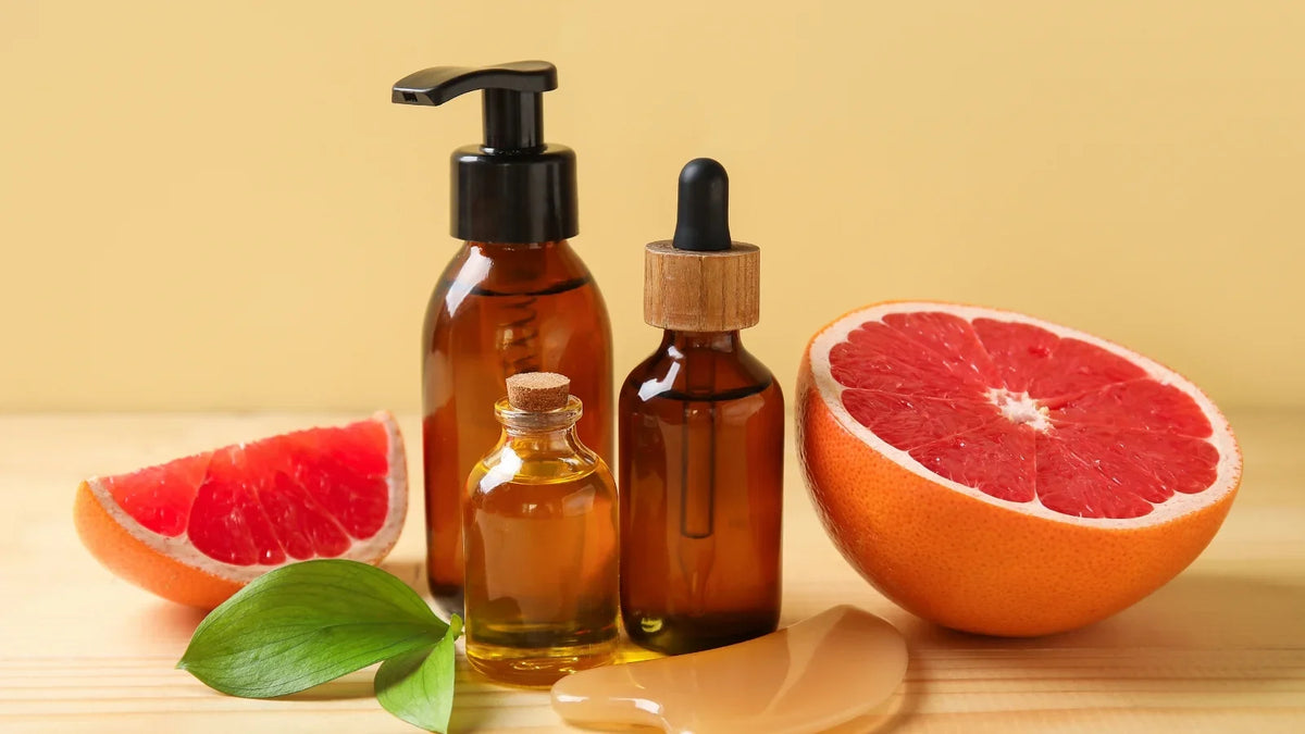 Amber bottle of grapefruit essential oil beside fresh pink grapefruit