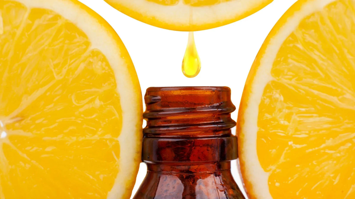 Amber bottle of sweet orange essential oil beside fresh oranges and peel