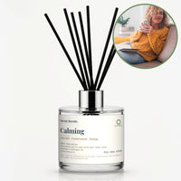 Calming Reed Diffuser by Seven Scents - glass bottle with a woman with a mug on a sofa