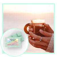 Hot drink being held with a close-up of evening ritual wax melts packaging on a soft gradient background