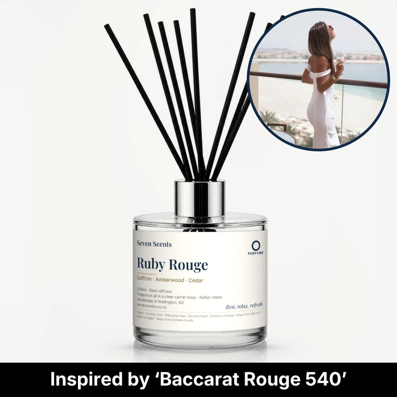 Ruby Rouge Reed Diffuser by Seven Scents - glass bottle with a woman in white on a seaside balcony