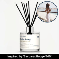 Ruby Rouge Reed Diffuser by Seven Scents - glass bottle with a woman in white on a seaside balcony
