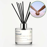 Sensual Reed Diffuser by Seven Scents - glass bottle with two hands holding against the sky