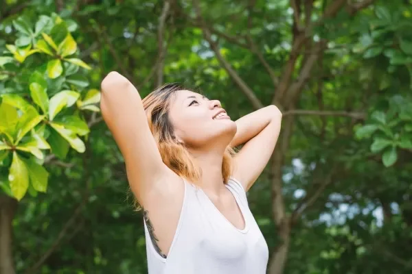 Woman with her hands clasped behind her head breathing in clean air in nature